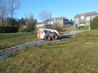 A skidsteer constructing a gravel road on a grassy hill.