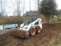 Skidsteer carries dirt in front of a pond