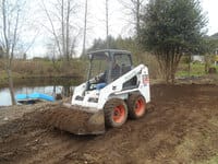 A skidsteer carries dirt beside a lake