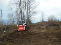 A skidsteer carries dirt up a hill.