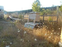 A wooden beehive stands behind some tall grass.