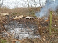 A pile of dead brush burns beside a small lake.