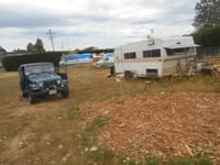 An RV trailer is parked in a field beside a Jeep.