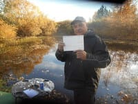 Richard holds a Vancity cheque in front of a small lake.