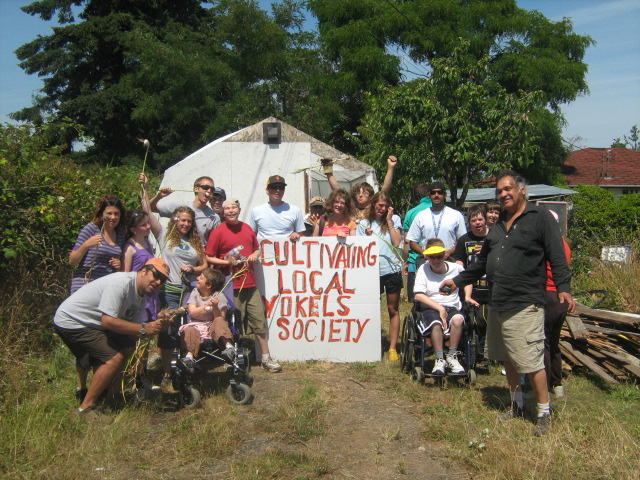 Friends in the garden standing around a sign for the Cultivating Local Yokels Society.